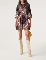 Vestido corto de manga larga con estampado estilo paisley en tonos azul marino, rojo y crema. Presenta un escote redondo con cordones ajustables, cintura elástica y mangas abullonadas.