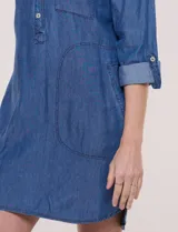 Vestido camisero blanco de rayón, con cuello con solapa, escote en V y pechera de abertura frontal con botones. Presenta un bolsillo delantero, bolsillos laterales aplicados y mangas largas con puño de largo regulable con presilla y botón. Cuenta con calce holgado y caída ligera, con ruedo irregular más largo en la parte trasera.