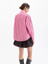 Camisa blanca de poplin con fit holgado, cuello con broche metálico y mangas largas con puños abotonados. Presenta un patrón de rayas verticales formadas por bordados de boquitas.