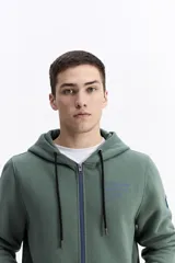 Campera con capucha y cierre frontal, color verde musgo, con cordones negros y cierre a contratono azul. Presenta un pequeño estampado en color azul en el pecho.