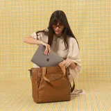 Cartera tipo tote bag color marrón tostado de símil cuero, con doble asa corta de mano y correa larga ajustable y desmontable. Cuenta con bolsillos frontales y traseros con cierre, bolsillos laterales abiertos y un amplio compartimento principal.