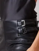 Pantalón de cuero sintético negro, de corte recto y tiro alto. Presenta cintura con hebillas laterales regulables y cierre frontal.