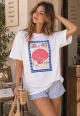 Remerón blanco de corte oversize con estampado frontal de una estampilla con concha marina y la inscripción 'La Dolce Vita'.
