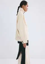 Chaqueta de algodón estilo denim, de diseño oversize, color beige, con cuello alto, manga larga, bolsillos de parche con solapa y cierre frontal de botones oscuros.