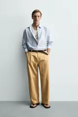 Pantalón chino straight fit de corte recto y holgado, color tostado, con pliegues frontales en la cintura, bolsillos laterales y cierre con cremallera y botón.