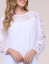 Blusa blanca de gasa liviana con forro interno en el cuerpo, de estilo boho-chic y silueta semi holgada. Presenta escote redondo con canesú de encaje calado en el frente y mangas largas con paneles longitudinales de encaje.