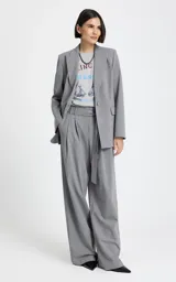 Blazer gris de sastrería con diseño entallado, cuello con solapas clásicas, hombros estructurados y mangas largas. Presenta bolsillos delanteros con solapa y un cinturón a juego con hebilla metálica para ajustar la cintura.