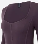 Body de manga larga confeccionado en poliamida y elastano, con diseño seamless y escote cuadrado. Presenta costuras verticales frontales que simulan un estilo corset y cierre con botones de presión en la entrepierna.