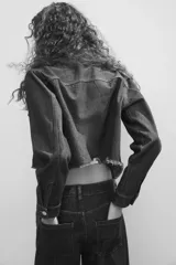 Campera cropped de denim de algodón rígido, color azul, con cuello, cierre frontal de botones y hombros caídos. Cuenta con bolsillos superiores con solapa y botón, puños abotonados y dobladillo deshilachado.