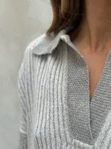 Sweater de punto acanalado color gris, con cuello polo y escote en V. Diseño holgado con mangas largas y aberturas laterales en el dobladillo.