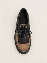 Mocasín de cuero con diseño bicolor en negro y marrón, con detalle de flecos sobre el empeine, cordones y suela track cosida.