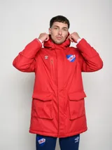 Parka larga de abrigo color azul marino, con capucha, cierre frontal, bolsillos con solapa y bolsillo superior con cierre. Presenta el logo de Umbro y el escudo del Club Nacional de Football.