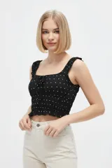 Musculosa de viscosa negra con estampado de lunares blancos, tirantes anchos con volados sutiles, escote cuadrado con cordón ajustable en el centro y cuerpo con punto smock elastizado.