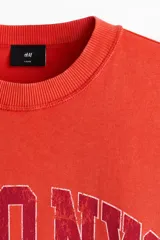Remera de algodón en color rojo, con cuello redondo acanalado, mangas cortas y hombros caídos. Presenta un estampado frontal con la leyenda "SOHO NYC ATH DEPT".