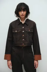 Campera de jean cropped color marrón oscuro, con costuras en contraste color beige, bolsillos con solapa, botones metálicos y puños rebatidos color marrón claro.