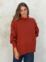 Sweater de lana color terracota, con cuello alto y detalles de volados en el cuello, hombros y puños.