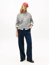 Sweater gris de tejido trenzado con cuello redondo y manga larga, confeccionado en algodón orgánico. Presenta un logo script TH gráfico bordado en color blanco en el centro del pecho.