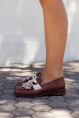 Zapato mocasín de cuero color marrón, con detalle de antifaz con aplique de cuero con estampado animal print y flecos.