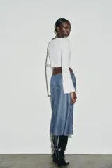 Camiseta de cuello barco y manga larga con diseño asimétrico en el bajo. Presenta un corte entallado con cierre lateral mediante cremallera oculta.