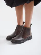Botinetas tipo Chelsea de cuero marrón, con paneles laterales elásticos y detalle de textura símil reptil en el talón. Poseen suela plana de goma negra y tirador trasero.