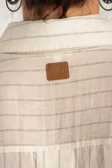 Camisa de manga larga con patrón de rayas sutiles, corte holgado, cuello camisero, cierre frontal con botones y un bolsillo aplicado en el pecho.