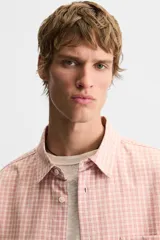 Camisa de corte relajado confeccionada en algodón, con estampado de cuadros pequeños en tonos rosados. Presenta cuello solapa, manga corta y bolsillo plastrón en el pecho con cierre frontal de botones.