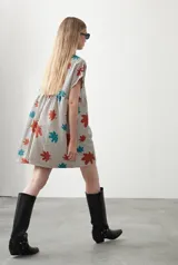 Vestido corto de silueta amplia con corte bajo busto, cuello a la base y mangas cortas. Presenta un estampado de lunares negros sobre fondo beige claro.