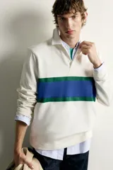 Remera polo de manga larga de corte regular fit, confeccionada en algodón color blanco crudo. Presenta cuello solapa blanco, cierre frontal con botonadura oculta y una franja horizontal ancha en el pecho en color azul y verde.