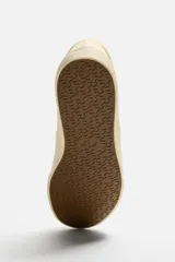 Zapatilla slip-on negra de tejido de algodón con elásticos laterales y suela color crema.