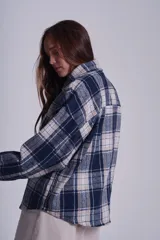 Sobrecamisa de franela color beige con estampado a cuadros en tonos marrones y azules, de corte holgado, con cuello clásico, cierre abotonado y bolsillos delanteros con solapa.