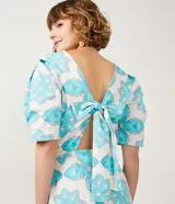 Vestido corto blanco con estampado de flores y corazones en color celeste, de corte recto, con mangas abullonadas y lazo en la espalda.