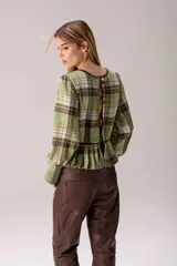 Blusa de tartán con diseño versátil, confeccionada en tela escocesa con detalles en cuero de oveja. Presenta cuello alto con forro de piel sintética, mangas largas con puños de cuero y piel, y un ruedo tableado con ajuste de cinturón de cuero en la cintura.