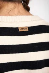 Sweater de punto con diseño a rayas horizontales en color negro y crema, de corte oversize. Presenta cuello redondo, mangas largas con puños acanalados y un detalle de borde inferior en color cobre con acabado brillante.