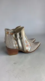 Bota de caña corta de cuero en tonos natural y dorado light, con diseño pintado a mano y puntera fina. Cuenta con taco bloque de madera y doble cierre lateral con tiradores personalizados.