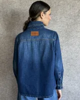 Sobrecamisa de denim azul con cuello camisero, cierre frontal con botones, mangas largas con puños abotonados y dos bolsillos con solapa en el pecho.