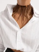Gargantilla de cinta marrón satinada con tachas metálicas oscuras y flecos de plumas colgantes en tono marrón.