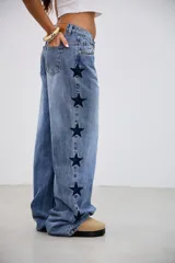Pantalón de jean tiro medio con corte recto y holgado, presenta bordados de estrellas oscuras a lo largo de los laterales externos.