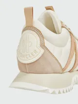 Zapatillas Moncler modelo Pacey, confeccionadas en una combinación de cuero y gamuza en tonos crema y beige. Presentan un diseño de paneles con cordones al tono y suela de goma.
