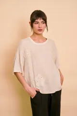 Blusa holgada color beige con mangas cortas y cuello redondo. Presenta apliques bordados con detalles de perlas y lentejuelas en el frente.