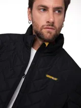 Campera puffer negra Caterpillar con diseño acolchado en chevrón, cuello alto y cierre frontal completo. Presenta el logo de la marca bordado en amarillo en el pecho.