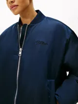 Campera bomber de satén azul marino con acabado repelente al agua y diseño acolchado. Presenta cuello estilo béisbol de punto canalé, cierre frontal de cremallera y logo de Tommy Hilfiger bordado en fuente script en el pecho.