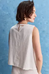 Top blanco sin mangas, con cuello redondo, diseño cruzado en el frente y cierre con botones en el hombro.