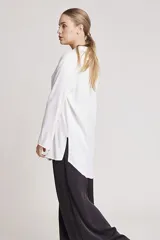 Camisa blanca de satén con cuello clásico, cierre frontal con botones y mangas largas.