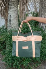 Bolso tipo tote de lona roja con detalles en cuero natural, incluyendo asas, correas decorativas y parche con logo de la marca Sierra Mora.