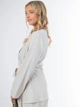 Conjunto de dos piezas confeccionado en lino color beige, compuesto por un pantalón de corte recto y un blazer cruzado con lazo ajustable en la cintura y escote en V.