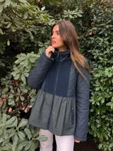Campera de silueta evasé, color azul marino, con cuello alto, cierre frontal y bolsillos laterales. Presenta diseño combinado con mangas y parte superior capitoneadas, pechera lisa y recorte inferior con patrón a cuadros y frunces.