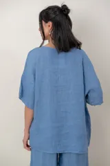 Blusa de lino color marrón oscuro, con escote redondo, mangas cortas amplias y detalle de alforzas verticales en el lateral derecho.