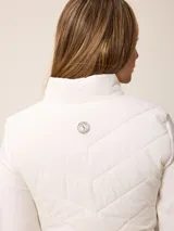 Campera acolchada con frente y espalda en tejido técnico, combinada con mangas y laterales de tejido liso. Presenta cuello alto, cierre frontal completo y bolsillos laterales. Incluye un pequeño detalle bordado en el pecho.