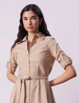 Vestido camisero blanco de algodón con cuello con solapa, delantera abotonada, mangas 3/4 regulables con presilla y botón, y cintura con lazo de ajuste.