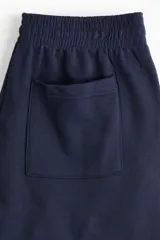 Jogging azul marino de corte holgado, tiro alto con cintura elástica fruncida y cordón oculto. Presenta piernas anchas con bolsillos laterales discretos y un bolsillo trasero abierto.